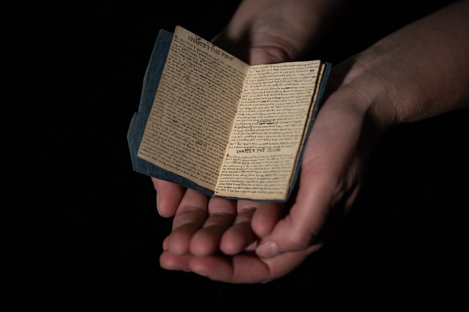 A curator cradles Visits in Verreopolis, a miniature handwritten book by Charlotte Brontë.